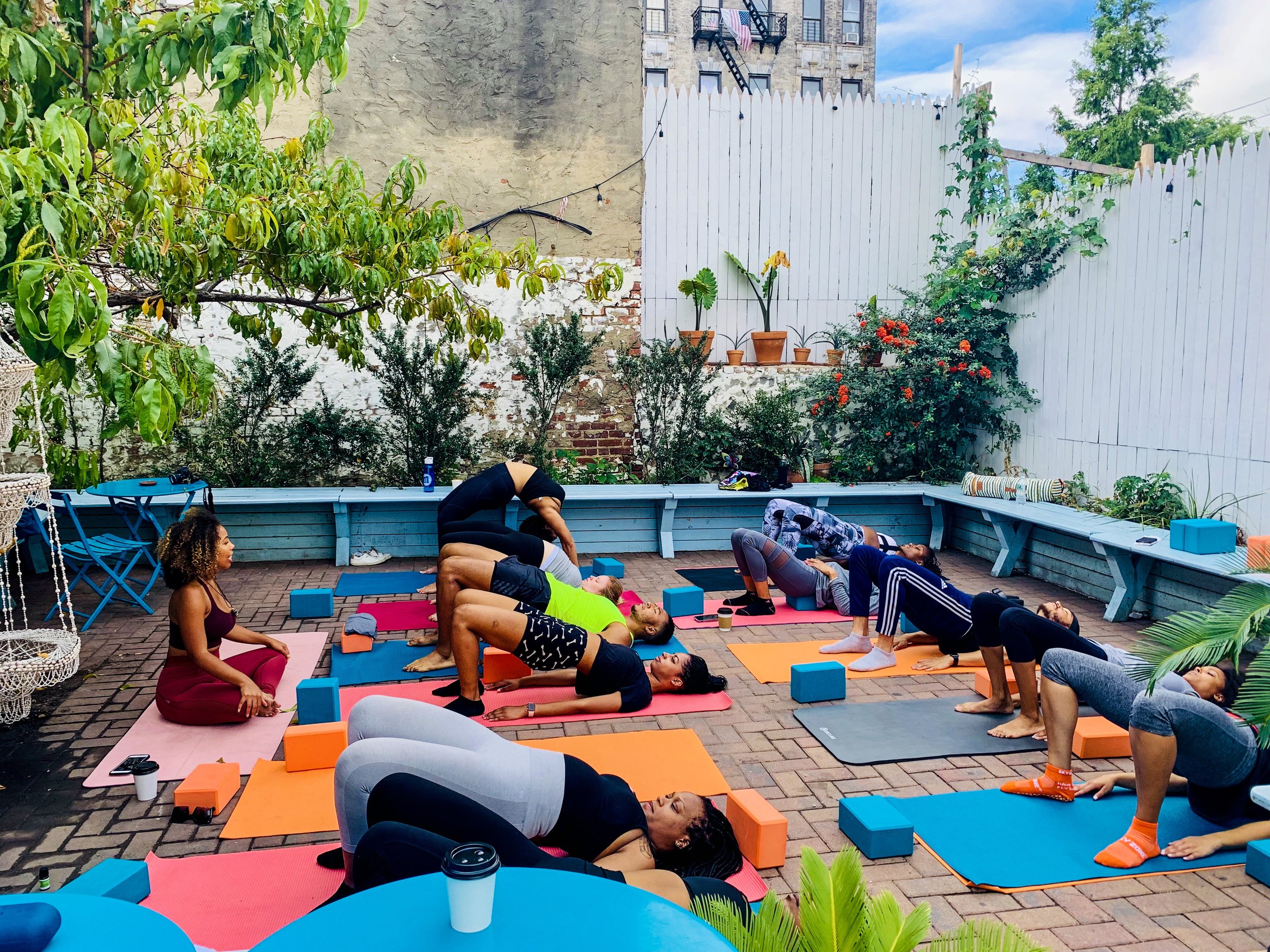Students in plank and stretch postures across colorful mats on a Brooklyn backyard patio
