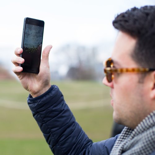 A visitor holds up a phone to view the Dandelion AR layer on Governors Island