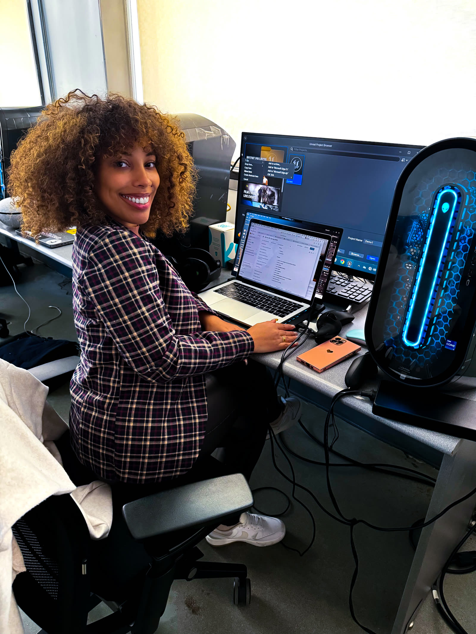 A snapshot from Najma's daily studio setup—laptop, external monitor running the Unreal Project Browser, an Alienware tower glowing alongside